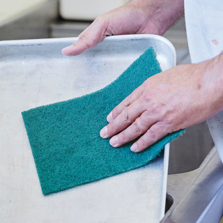 Green scourer pad being used to clean a metal tray.