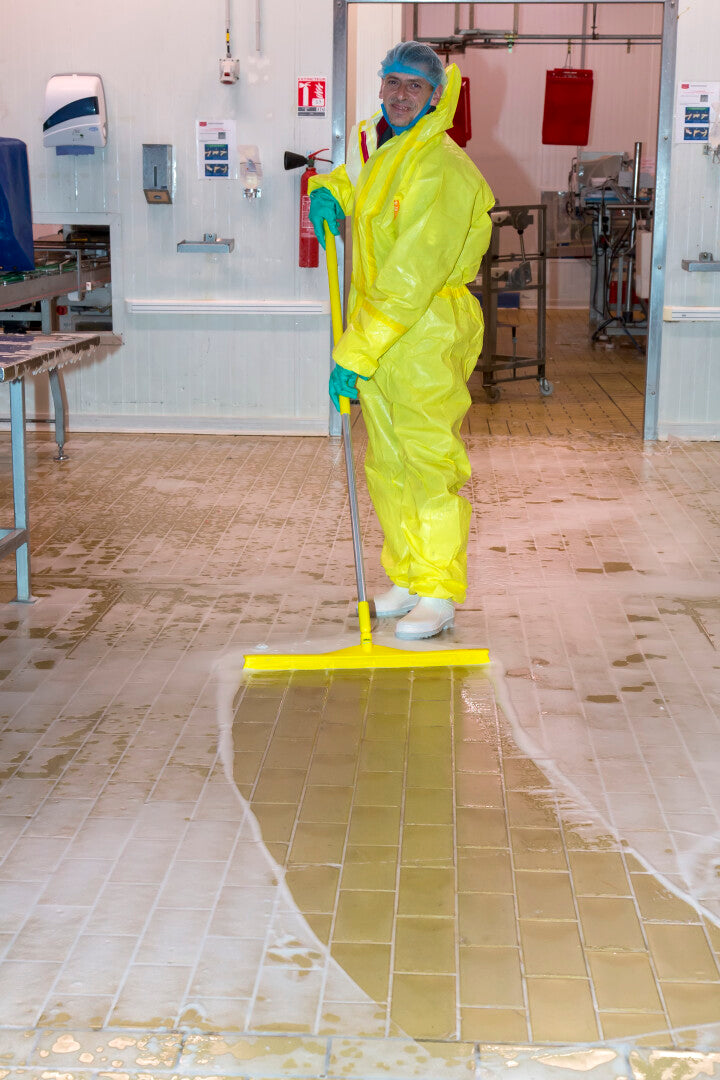 Person in yellow protective gear using a Vikan Ultra Hygiene Squeegee on a wet floor.