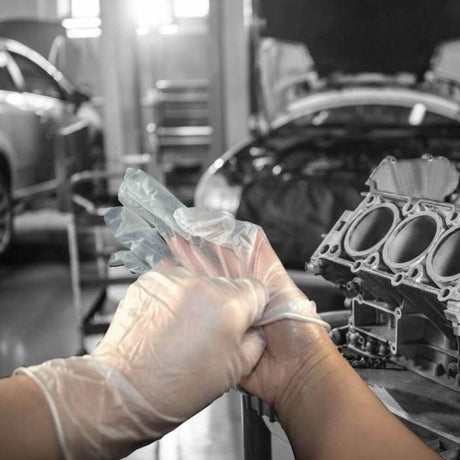 Hands putting on Jangro Professional Vinyl Powder Free Gloves in a workshop setting.